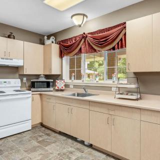 A modern kitchen with light wooden cabinets, a white stove, and a microwave under a large window with red curtains.