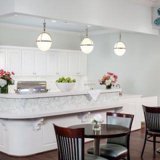 A modern kitchen with a marble countertop, pendant lights, and dining area featuring wooden chairs and a round table.