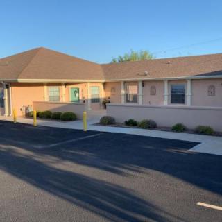 A small, single-story building with a parking lot in front, captured on a sunny day.
