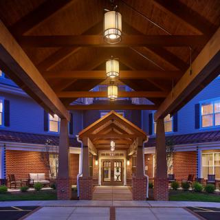 A warmly lit building entrance with a peaked wooden roof, captured during the evening.