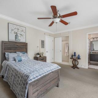 A modern bedroom with a wooden bed frame, ceiling fan, and neutral decor.