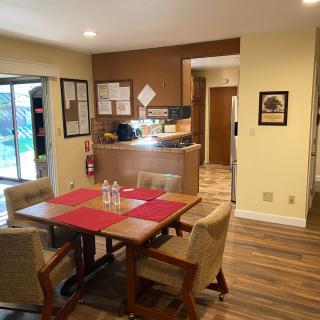 A cozy dining area with a table and chairs, adjacent to an open kitchen, featuring wood flooring and warm decor.