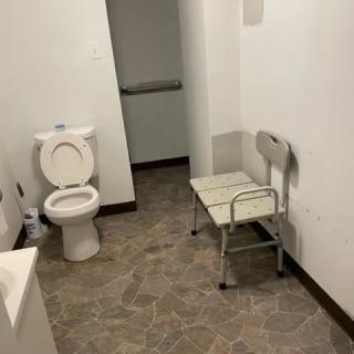 A simple bathroom setup with a toilet and a chair against white walls.