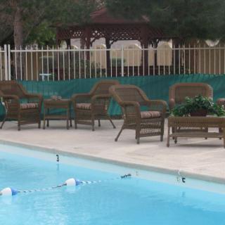 Outdoor pool area with patio chairs and a fence in the background.