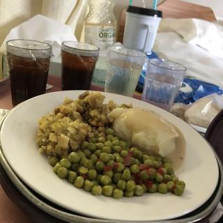 A meal consisting of chicken, peas, and stuffing served on a plate with drinks in the background.