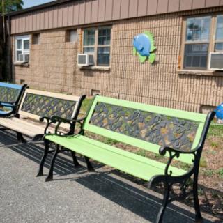 Outdoor benches placed against a brick building with windows and air conditioners.