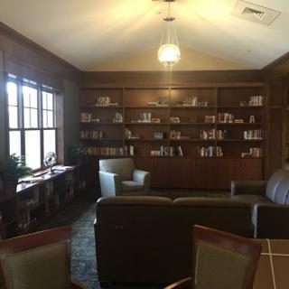 A cozy library room with bookshelves, armchairs, and warm lighting.