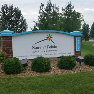 A sign for Summit Pointe Behavioral Healthcare is surrounded by bushes and trees.