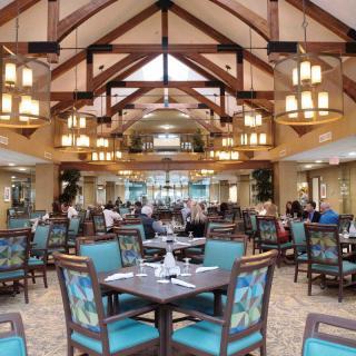 A spacious restaurant interior featuring wooden ceiling beams and elegant lighting, with neatly arranged tables and chairs.