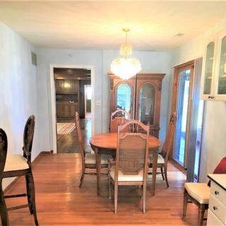 A cozy dining room featuring a wooden table, chairs, and a cabinet with a chandelier overhead.