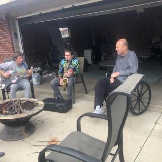 A casual music session in a driveway with friends playing instruments.