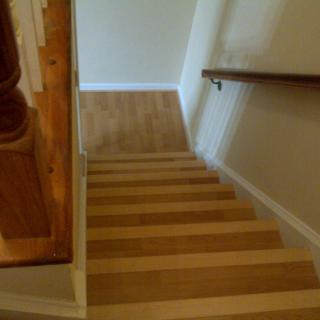 A view of wooden stairs leading down with a handrail on the right side.