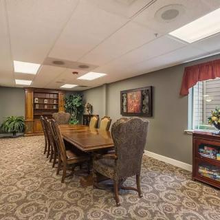 A well-furnished conference room with a large table and chairs, featuring a bookshelf, indoor plants, and decorative artwork.