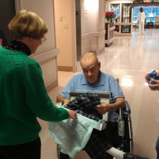 A heartwarming moment of gift-giving at a hospital, where a caregiver presents a surprise to an elderly man in a wheelchair.