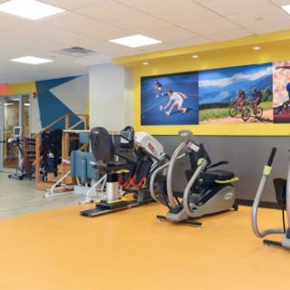 A well-equipped gym space featuring various exercise machines and a vibrant mural.