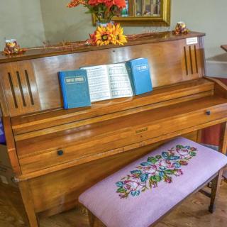 A wooden piano with open sheet music, accompanied by a floral-decorated bench, adorned with flowers on top.
