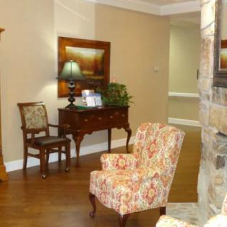A cozy living room with a patterned armchair, wooden furniture, a lamp, and decorative elements.