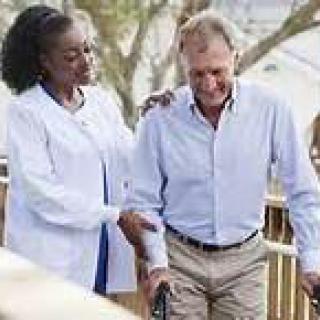 A caregiver assisting an elderly man during a walk outdoors.