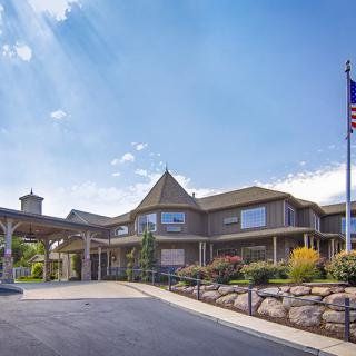 A large, multi-story building with a driveway in front and a flagpole, set against a clear blue sky.
