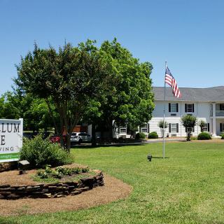 A white building with a sign on the lawn, surrounded by trees and grass, under a clear blue sky.