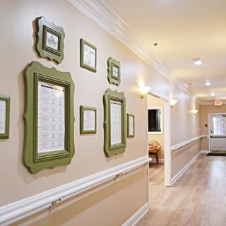 A well-lit hallway featuring decorative frames on the walls and a warm wooden floor.