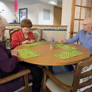 A group of elderly people playing bingo around a table in a community setting.