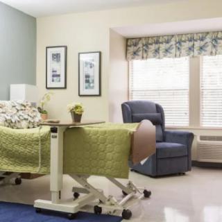 A hospital room with a bed, chair, and large window providing natural light.
