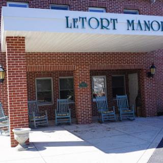 The entrance of Letort Manor, featuring a brick facade and rocking chairs for outdoor relaxation.