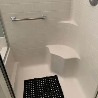 A bathroom shower with a built-in seat, towel rack, and floor mat.