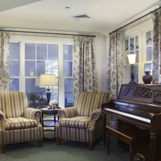 A cozy living room with a piano and striped armchairs by the window.