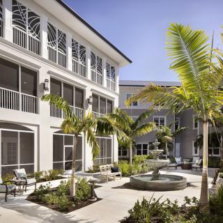 A modern courtyard with palm trees and a fountain, surrounded by buildings with outdoor seating.