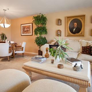 A cozy living room with a neutral color scheme, featuring comfortable seating, a coffee table adorned with decorative items, and a dining area in the background.