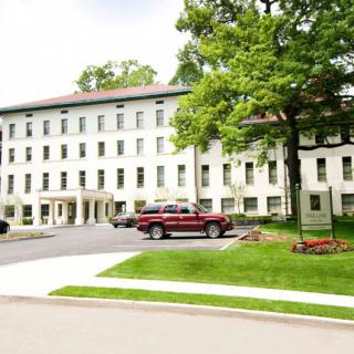 A multi-story building surrounded by trees and parked cars, with a neatly maintained lawn in the foreground.