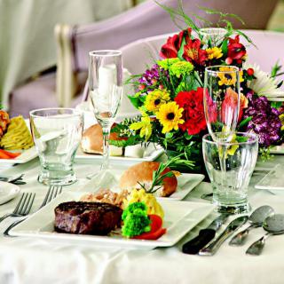 An elegantly set dining table with a steak dish and colorful flower centerpiece.