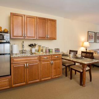 A compact kitchen and dining area featuring wooden cabinets, a small fridge, and a cozy table with chairs.