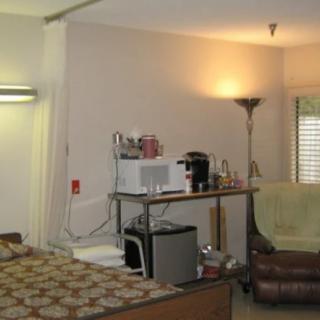 A cozy bedroom with a bed, chair, and small kitchen appliances.