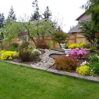 A beautifully landscaped garden with colorful flowers and lush greenery, bordered by a wooden fence.