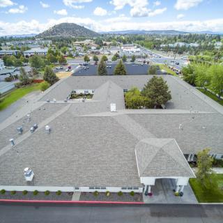 An aerial view of a large building surrounded by greenery and suburban landscape under a blue sky.