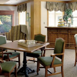 A cozy dining area with a wooden table, green upholstered chairs, and large windows letting in natural light.