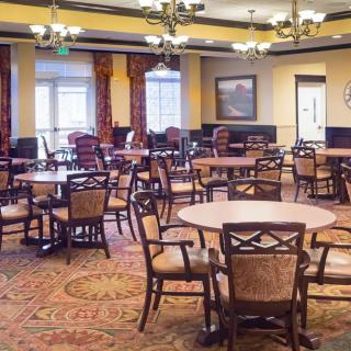 A spacious dining room with multiple tables and chairs, elegantly decorated with chandeliers and patterned carpet.