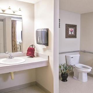 A clean and neatly organized bathroom with a sink, mirror, towel dispenser, and toilet.