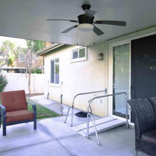 A covered patio featuring a ceiling fan, chairs, and a ramp leading to a sliding glass door.