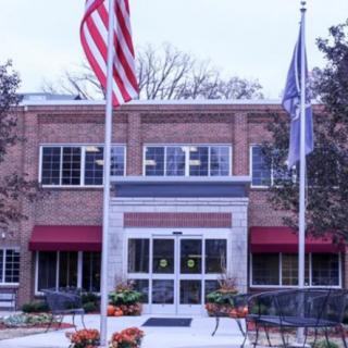 A brick building entrance with flags and outdoor seating.