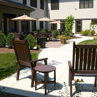 A serene courtyard featuring wooden chairs, patio umbrellas, and well-manicured gardens.