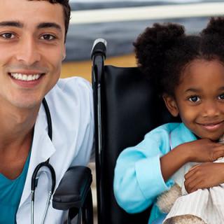 A doctor smiling with a young child in a wheelchair at a hospital.