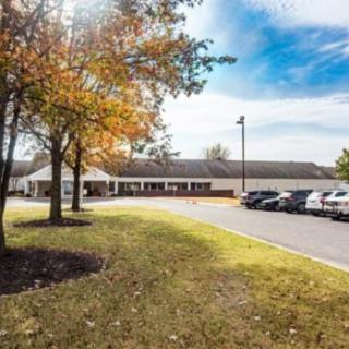 A wide view of a building with an adjacent parking lot and trees with autumn foliage under a blue sky.