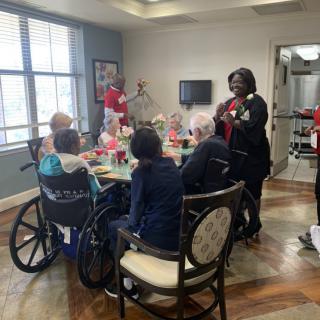 A group of seniors and caregivers gathered around a table at a nursing home.