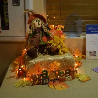 A charming autumn decoration featuring a scarecrow surrounded by colorful leaves and twinkling lights.