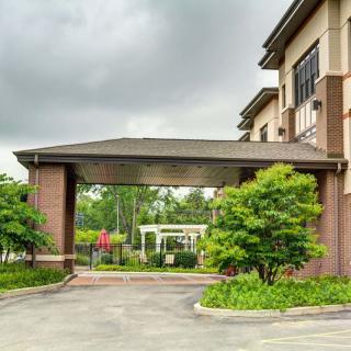 A building entrance with a covered driveway, surrounded by greenery under a cloudy sky.