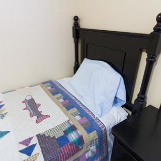 A neatly made bed with a colorful quilt and a light blue pillow.